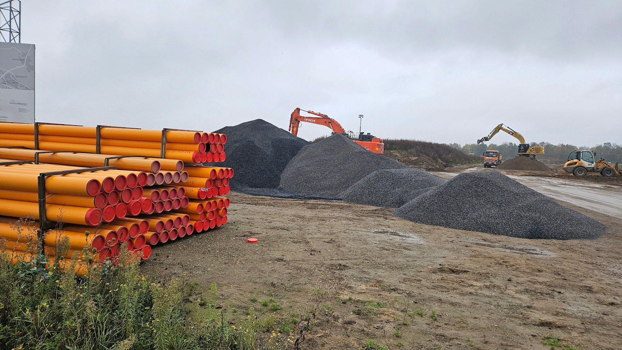 Zu sehen ist eine Baustelle mit Baggern, Schotterhaufen und Rohren.