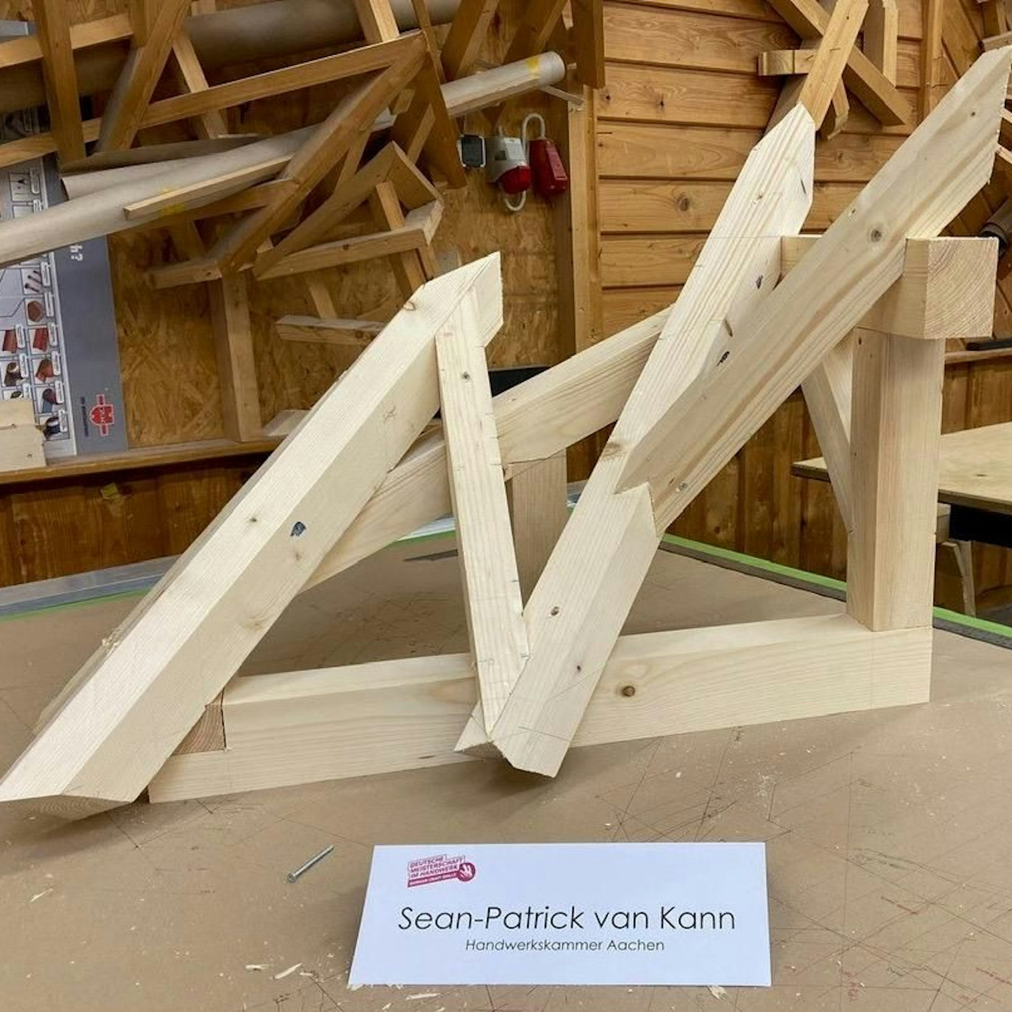 Werkstück im Wettbewerb der Zimmerer, davor liegt ein Namensschild mit der Aufschrift „Sean-Patrick van Kann, Handwerkskammer Aachen“.