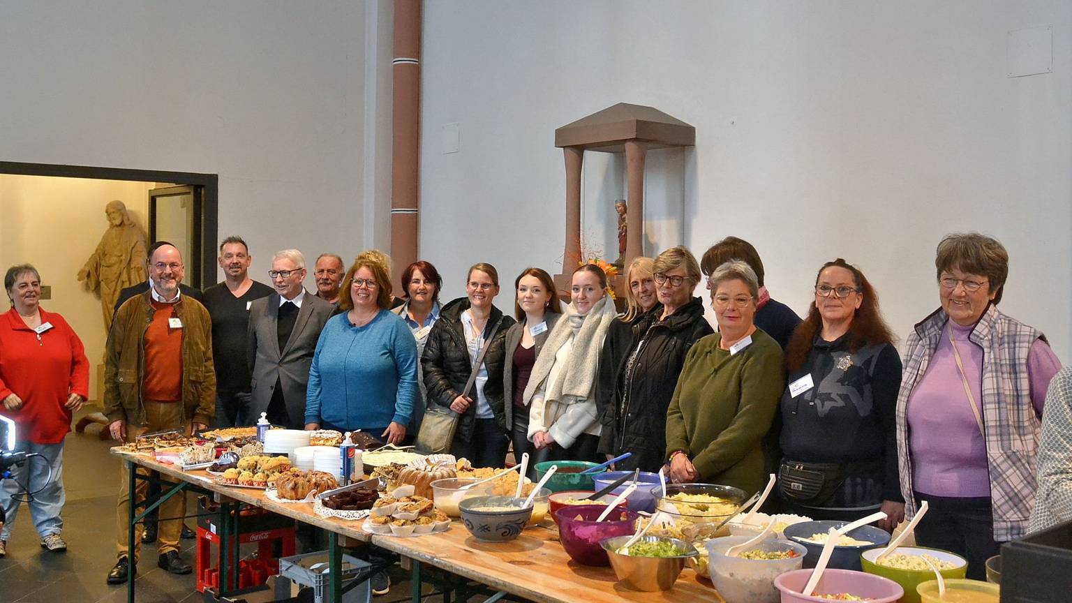 Zahlreiche Männer und Frauen stehen hinter einem langen Buffet-Tisch, auf dem viele Schüsseln mit Speisen stehen.