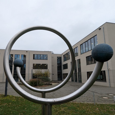 Das Foto zeigt eines der neuen Schulgebäude des Ernst-Mach-Gymnasiums hinter einem Sportgerät auf dem Schulhof.