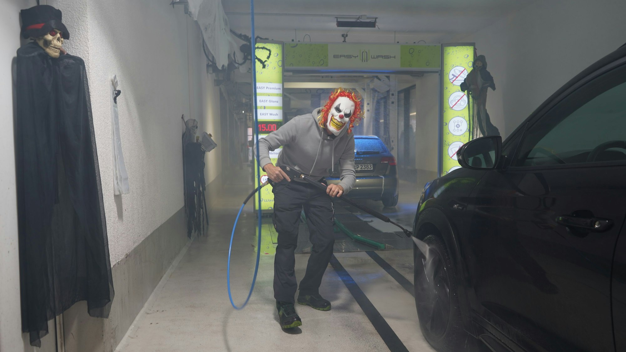 Das Foto zeigt einen Mann mit einer Clown-Maske, der ein Auto wäscht.