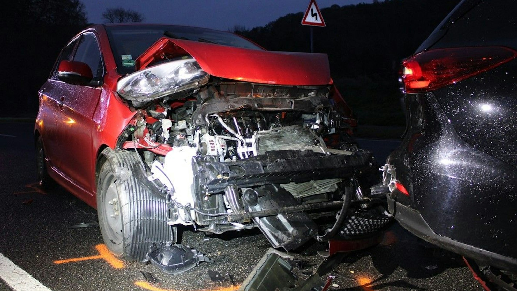 Ein schwer beschädigter roter Kia steht am Heck eines weiteren, ebenfalls beschädigten Fahrzeugs auf der Altenberger-Dom-Straße in Odenthal.