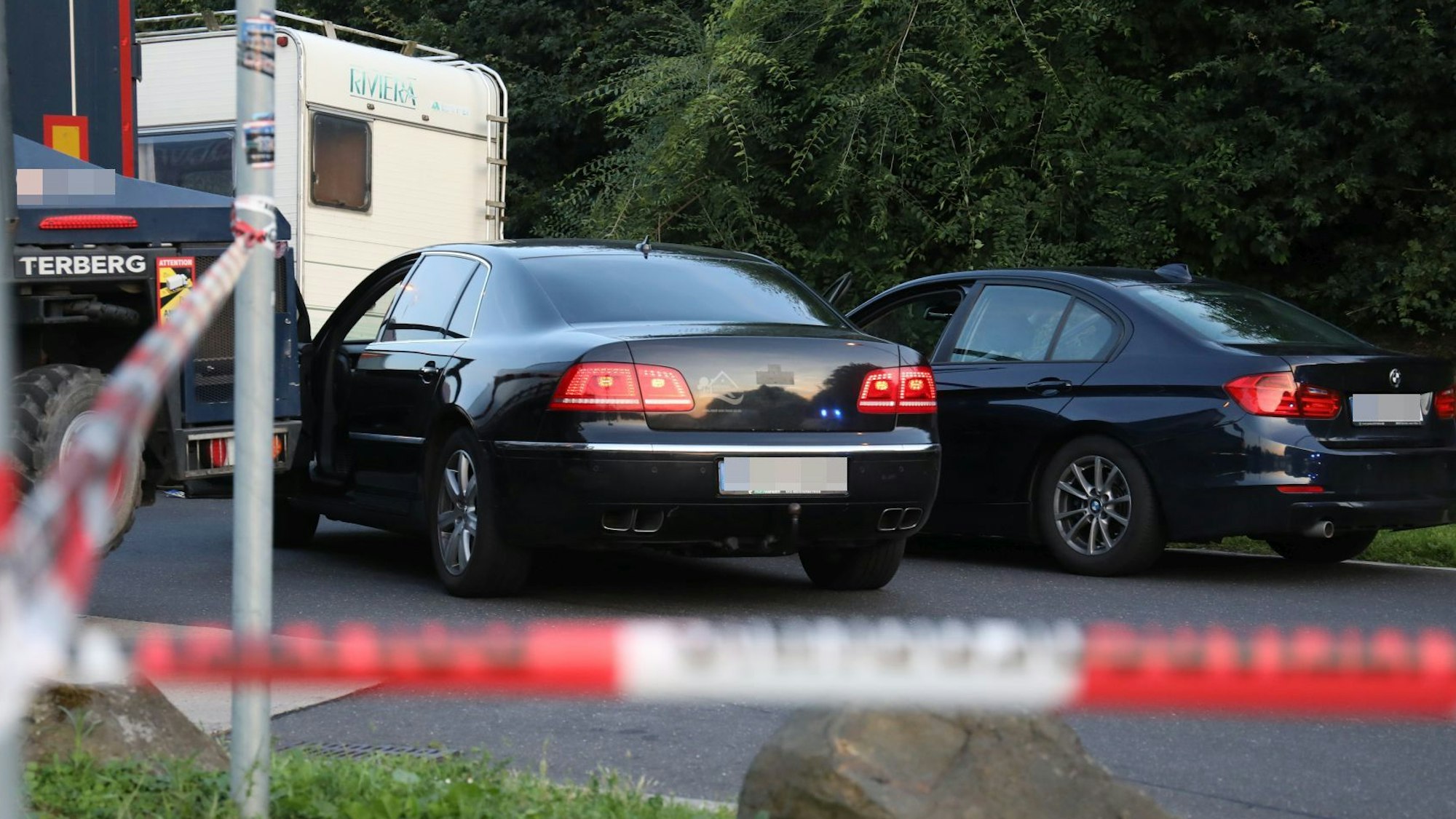 Ein rot-weißes Flatterband im Vordergrund, dahinter zwei Pkw und ein Wohnmobil.