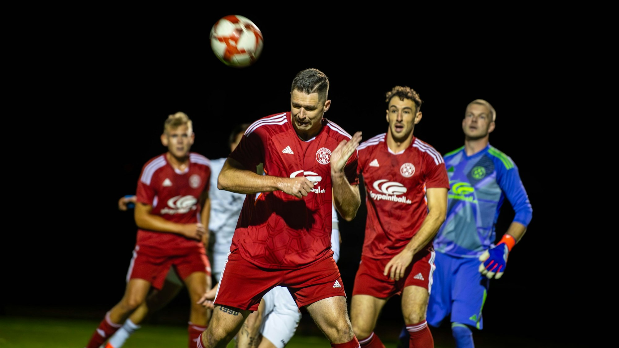 Ein Fußballer köpft einen Ball weg. Drei Mitspieler beobachten ihn dabei.