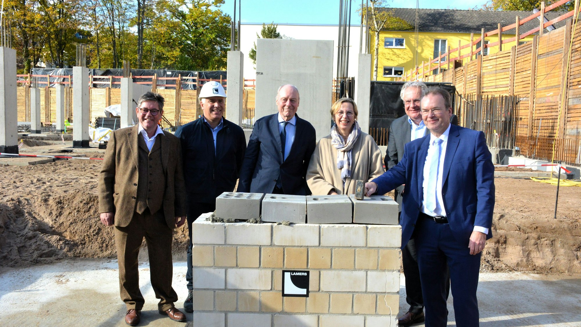 Fünf Männer und eine Frau stehen hinter einer hüfthoch gemauerten Wand.