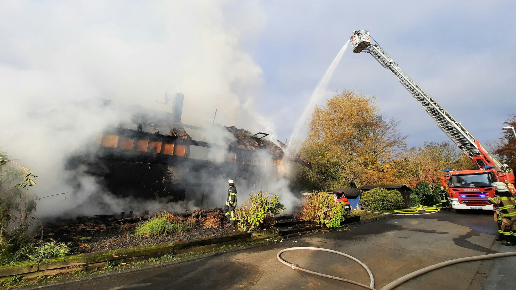 Eine Drehleiter der Feuerwehr neben einem Gebäude, aus dem dichter Rauch aufsteigt.