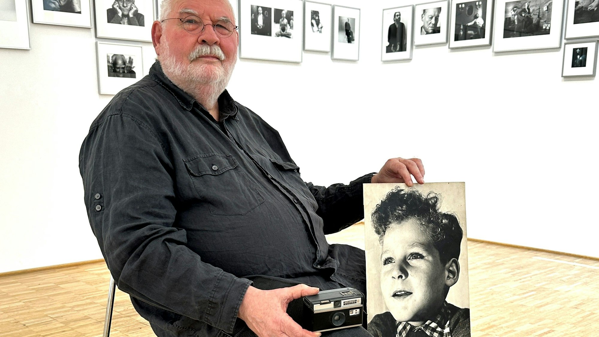 Der Fotograf Gerd van Rijn aus Nümbrecht mit der alten Instamatic und dem Porträtfoto seiner selbst als Junge. In seiner Heimatgemeinde ist ihm nun eine Ausstellung gewidmet.