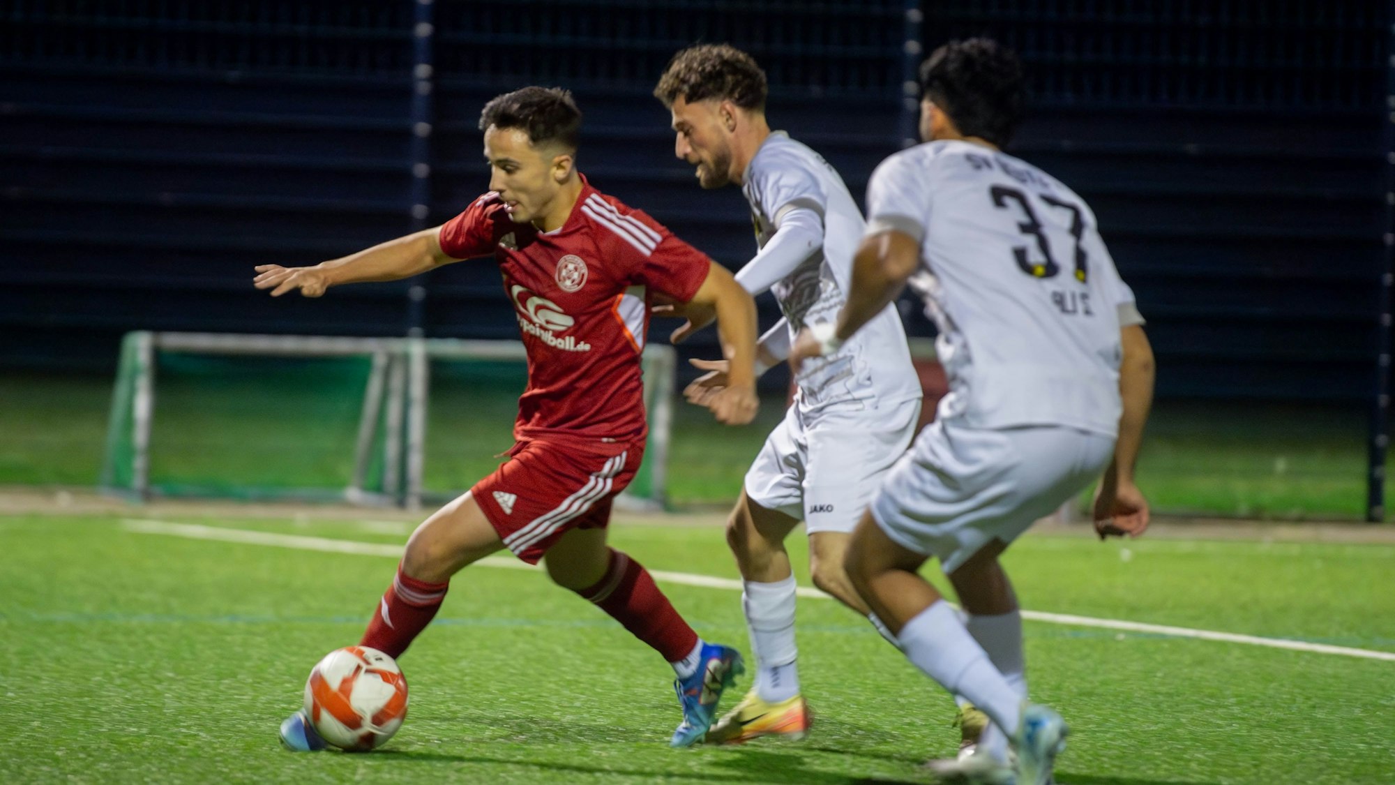 Ein Fußballer dribbelt mit dem Ball am Fuß, zwei Gegenspieler verfolgen ihn.