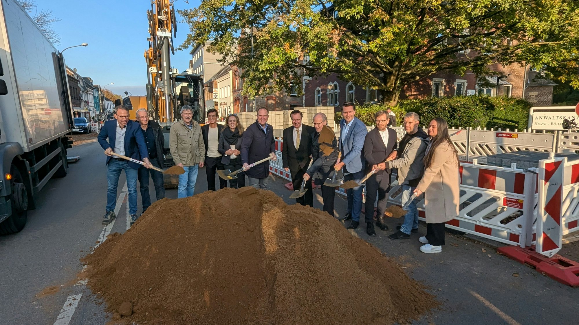 Das Foto zeigt eine Reihe von Menschen, die mit dem Spaten in einen Sandhaufen an der Baustelle auf der Luxemburger Straße stechen.