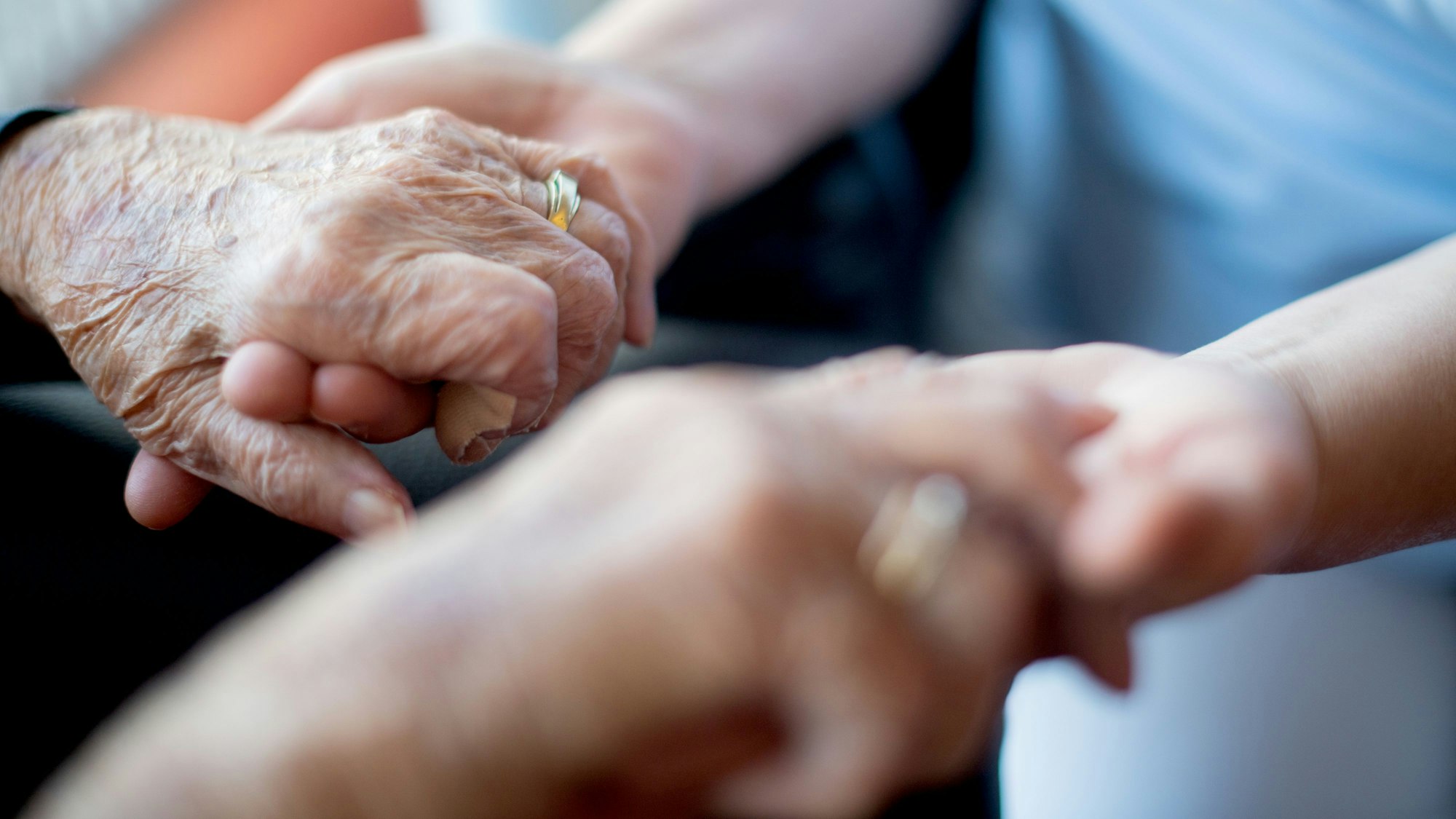 Eine junge Person hält die Hände einer älteren Person.