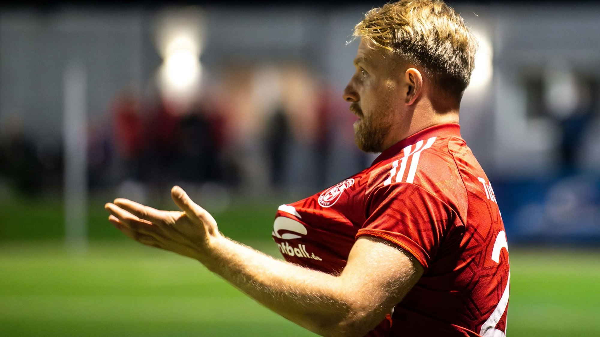 Ein Fußballer beschwert sich darüber, dass er am Trikot gezogen wurde. Da man die Hand, die am Trikot zieht, nicht sieht, scheint sich das Trikot wie von selbst zu bewegen.