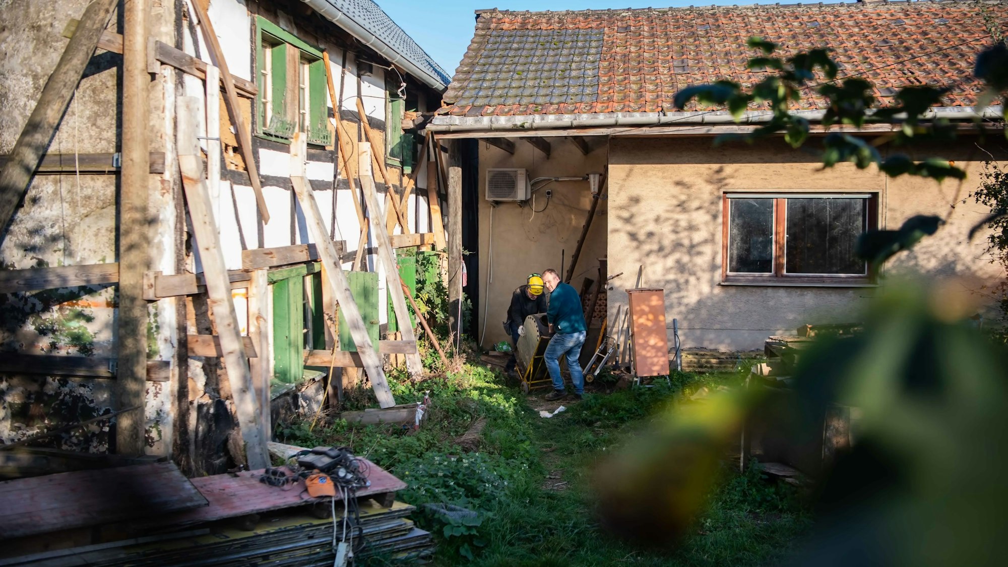 Das Bild zeigt zwei Helfer, die gerade einen Ofen aus dem Fachwerkhaus bei Lommersum wuchten.