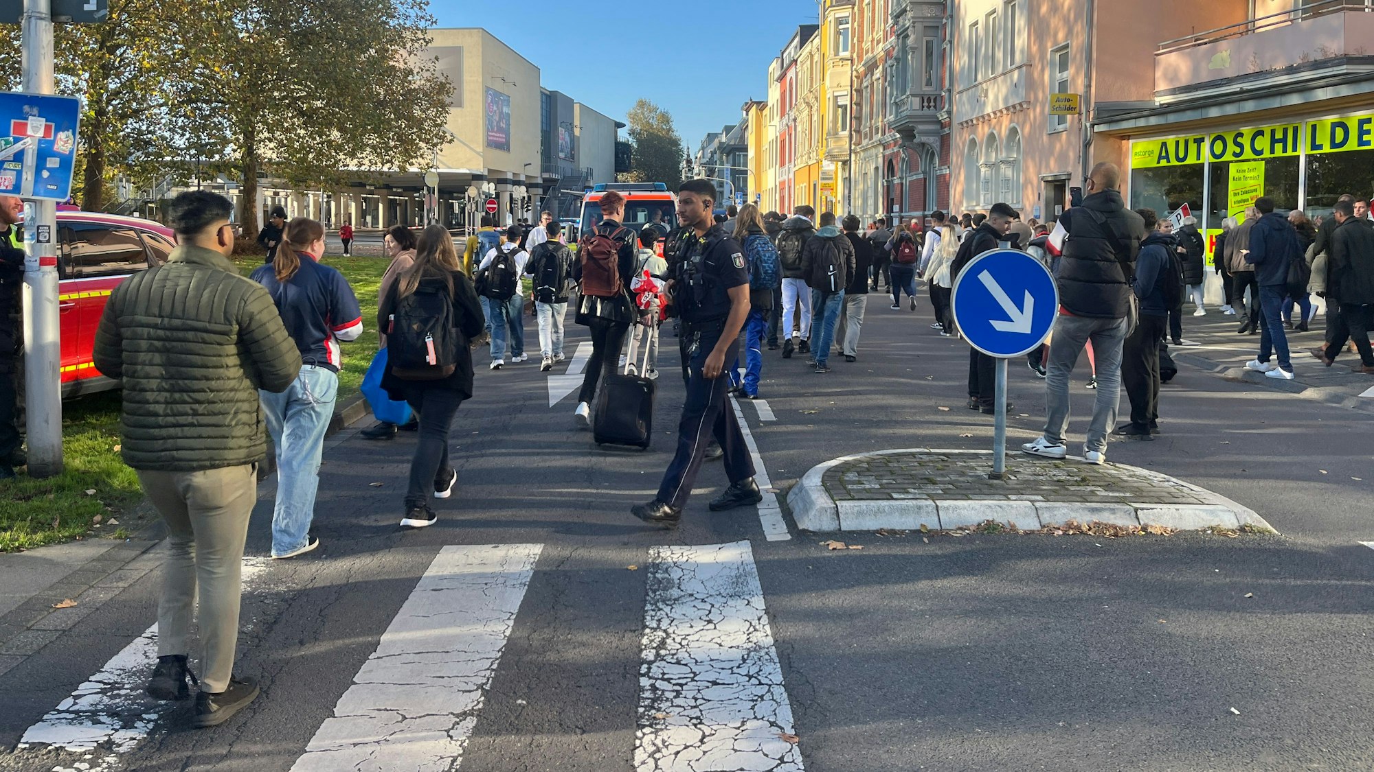 Menschen strömen über eine Straße zu einem Bahnhofsgebäude.