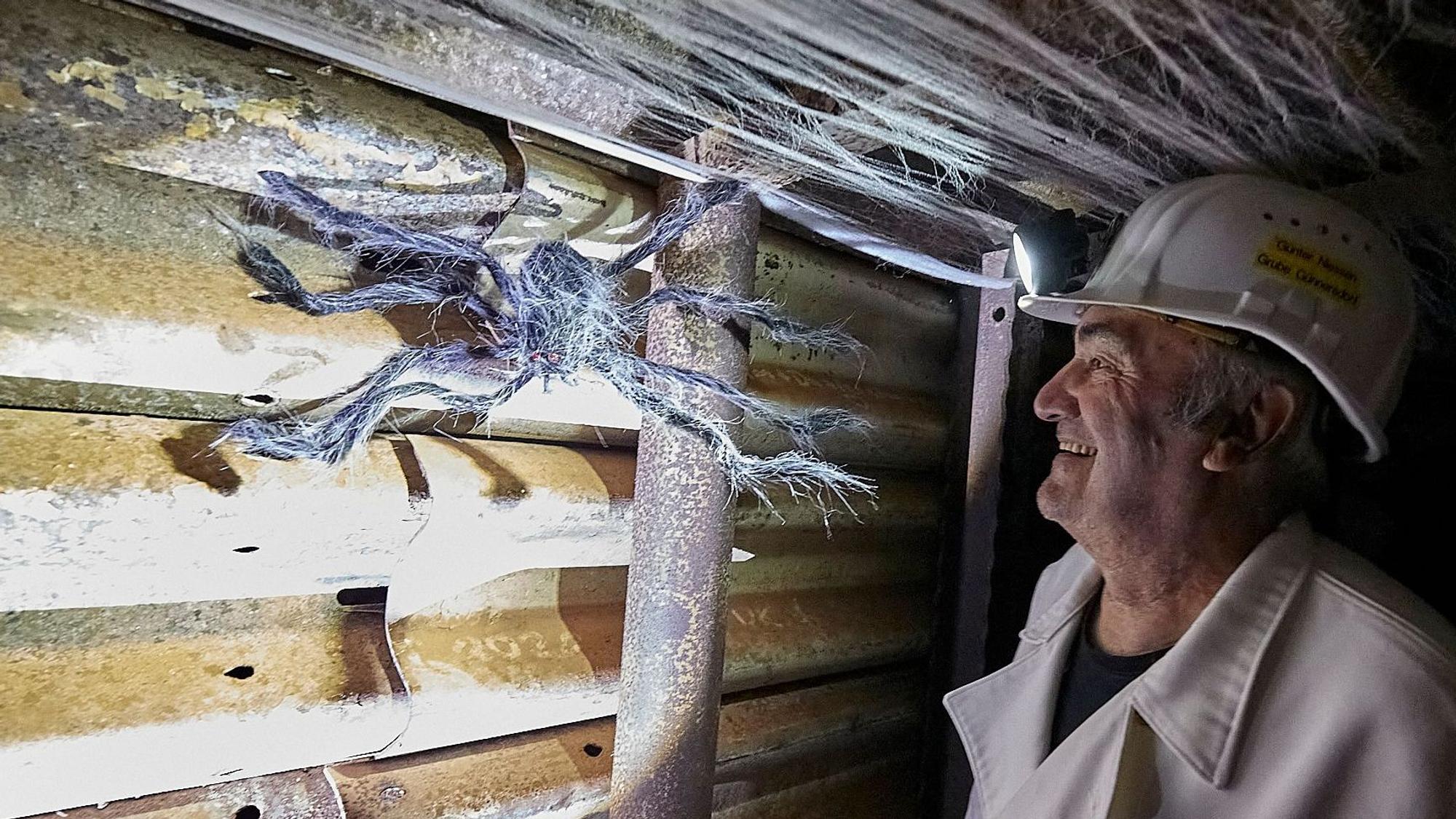 Günter Nießen trägt die weiße Kleidung eines Bergmanns und betrachtet Besucherbergwerk Grube Günnersdorf eine große Spinnenfigur, die als Halloween-Dekoration an der Wand angebracht ist.