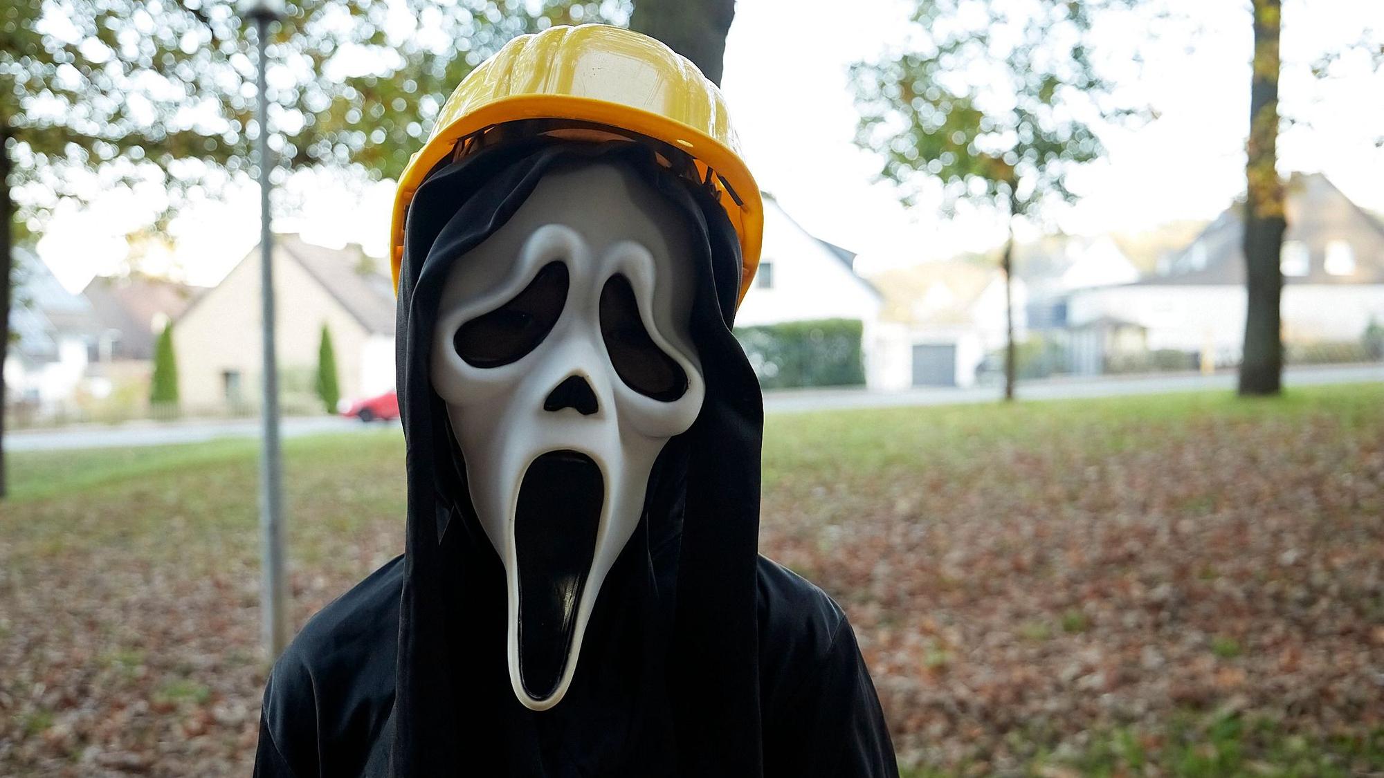 Ein Mädchen ist zu Halloween als Gruselbergmann mit Scream-Maske und gelbem Bauarbeiter-Helm verkleidet.