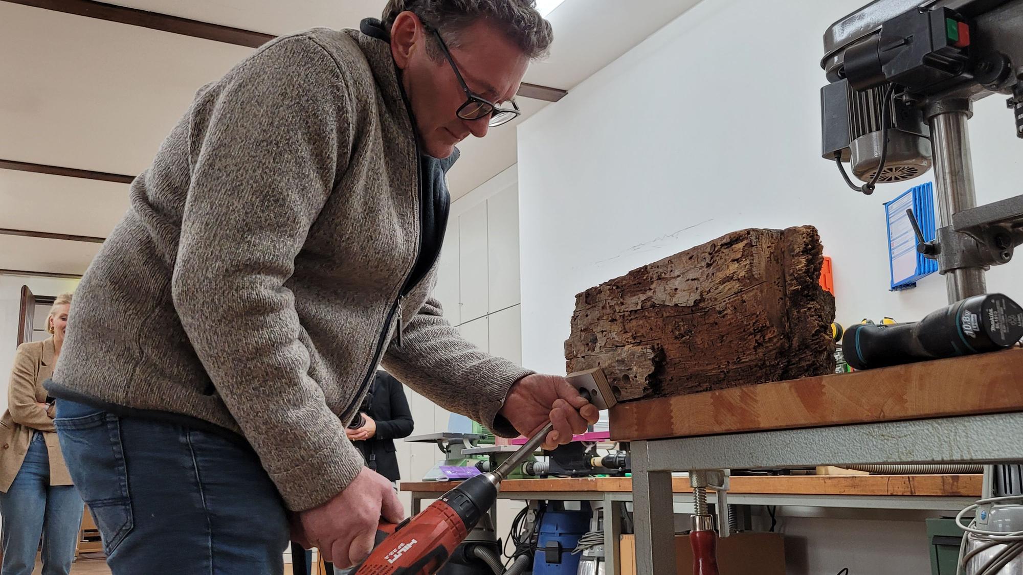 Ein Mann bohrt einen Holzbalken an.