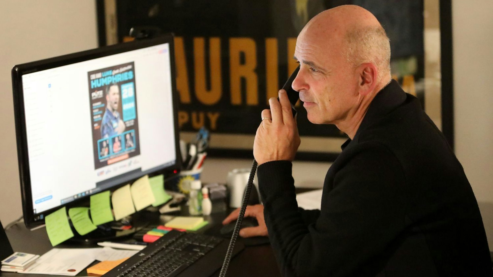 Ein Mann sitzt an einem Schreibtisch vor einem Computer und telefoniert.