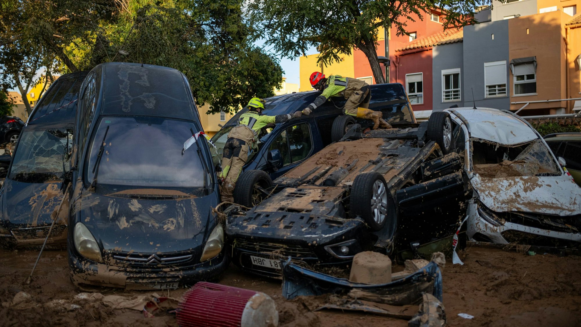 Zwei Feuerwehrleute arbeiten in einem von dem Unwetter betroffenen Gebiet und klettern über zerstörte Autos.