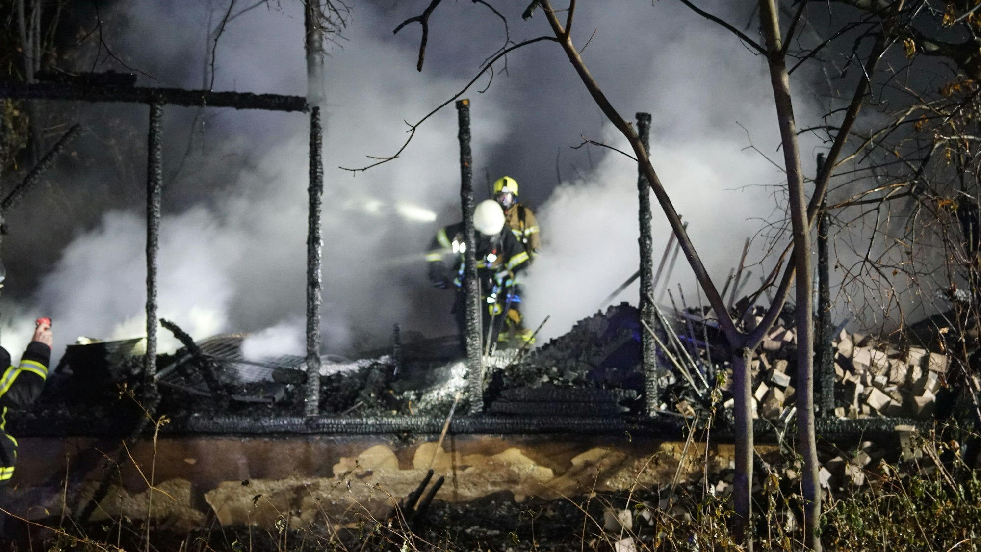 Zwei Feuerwehrleute gehen durch die Trümmer einer niedergebrannten Gartenhütte.