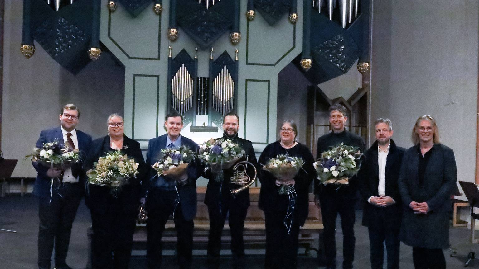 Acht Menschen schauen in Richtung der Kamera, sechs von ihnen halten Blumensträuße.