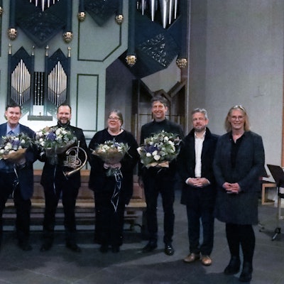 Acht Menschen schauen in Richtung der Kamera, sechs von ihnen halten Blumensträuße.
