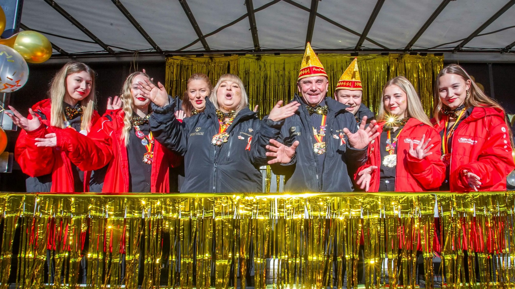Menschen mit Narrenkappen feiern auf einer Bühne.