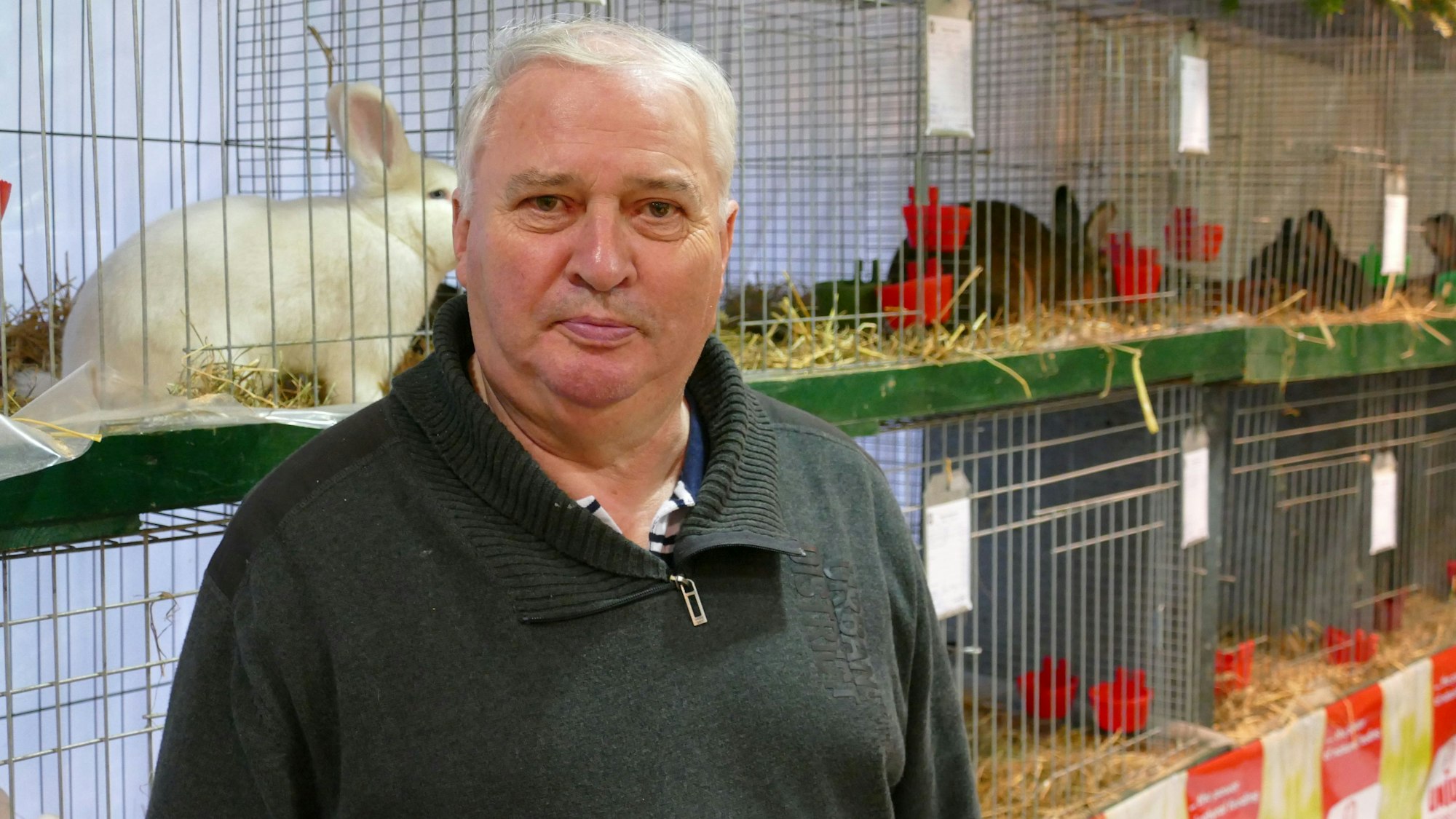Ein grauhaariger Mann steht vor Käfigen mit Kaninchen.