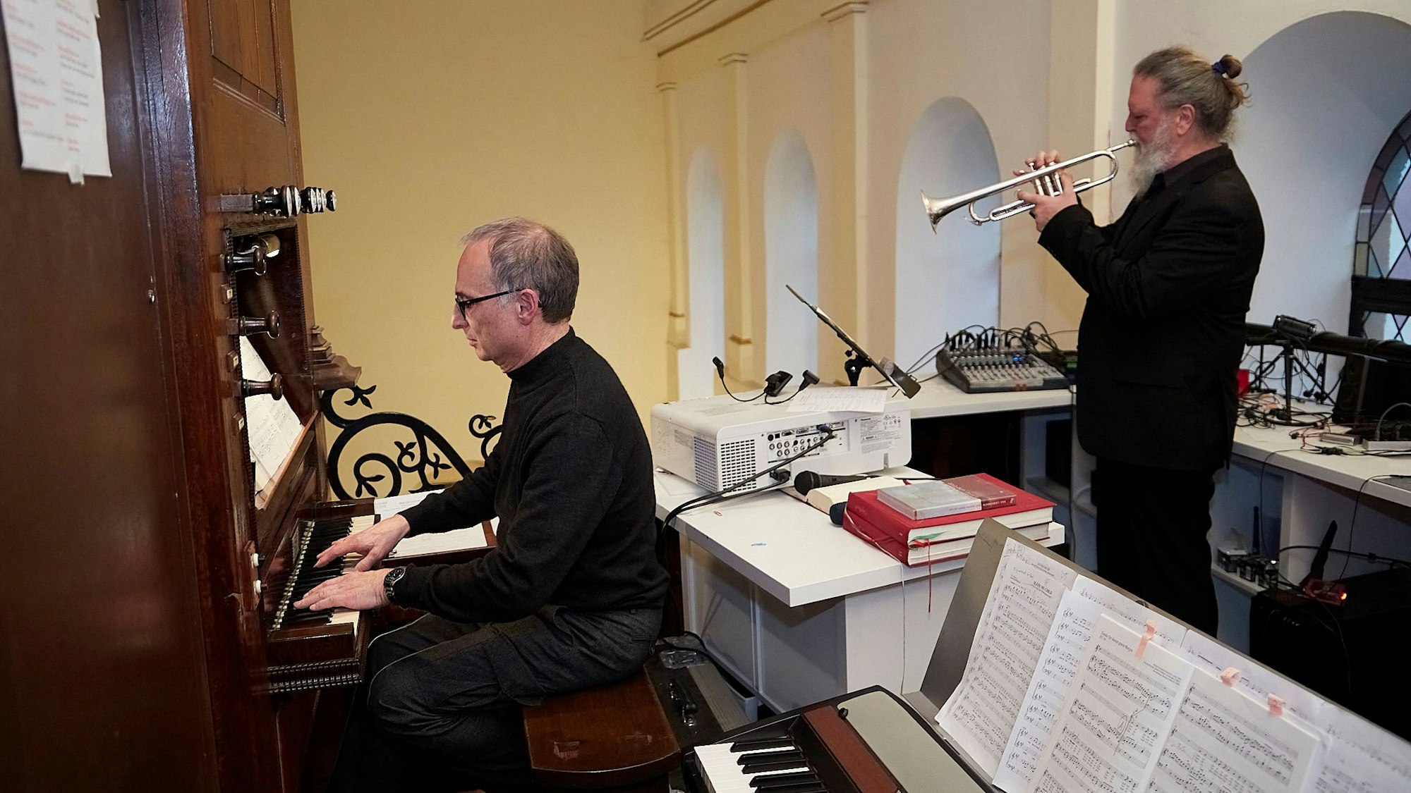 Ein Mann spielt an der Orgel, während ein anderer Mann Trompete spielt.