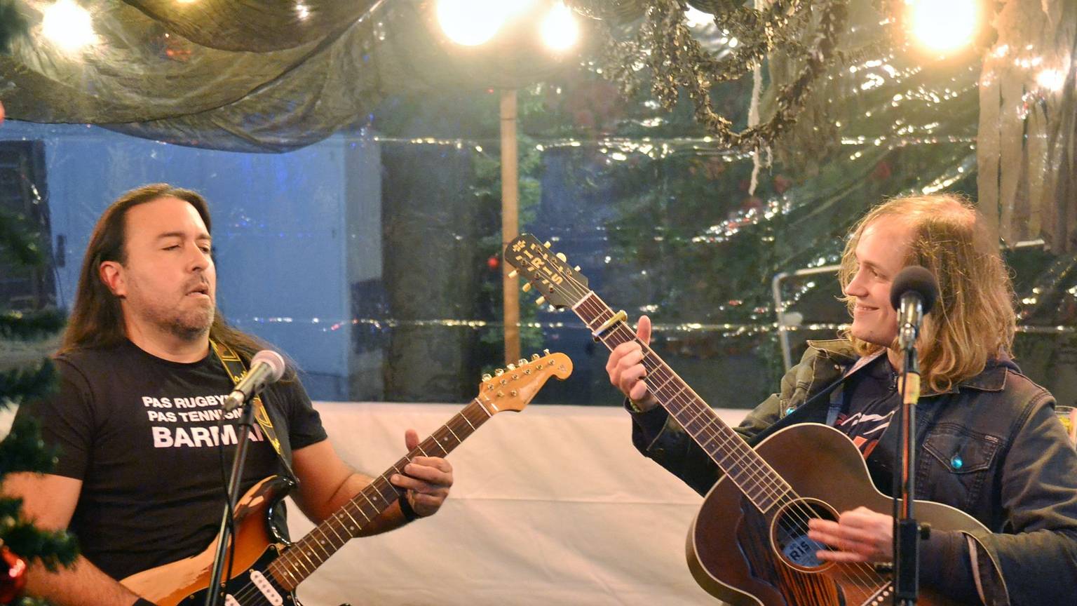 Zwei Männer spielen Gitarren hinter Mikrofonen und schauen sich an.