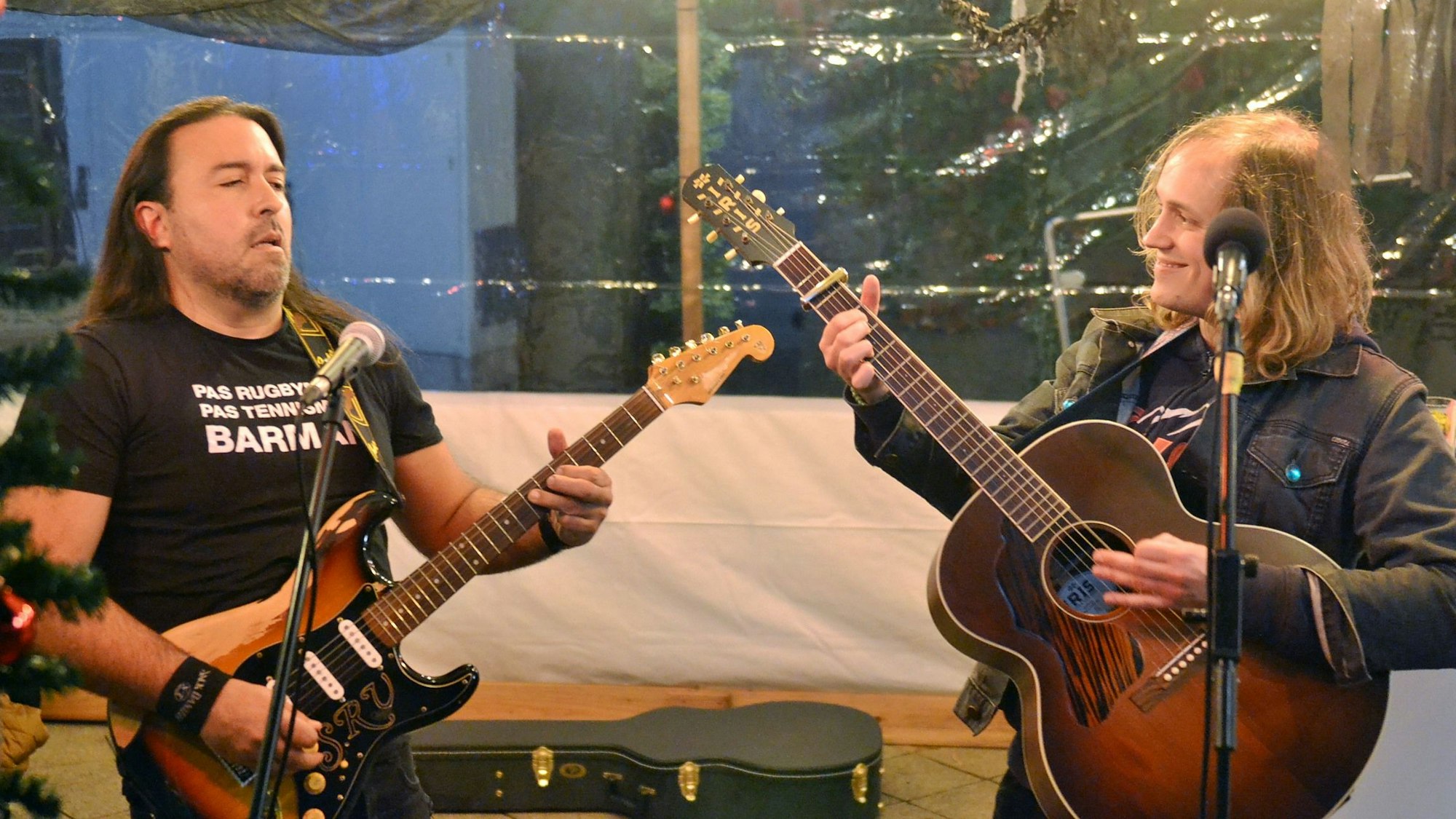 Zwei Männer spielen Gitarren hinter Mikrofonen und schauen sich an.