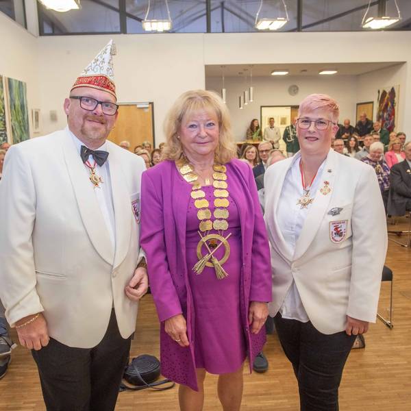 Eine Frau steht, mit einem goldenen Orden um den Hals, mit zwei Männern eines Karnevalsvereins beisammen.