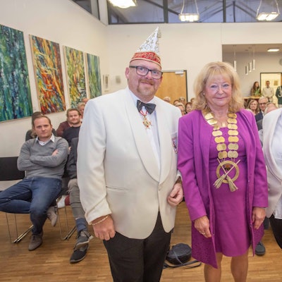 Eine Frau steht, mit einem goldenen Orden um den Hals, mit zwei Männern eines Karnevalsvereins beisammen.