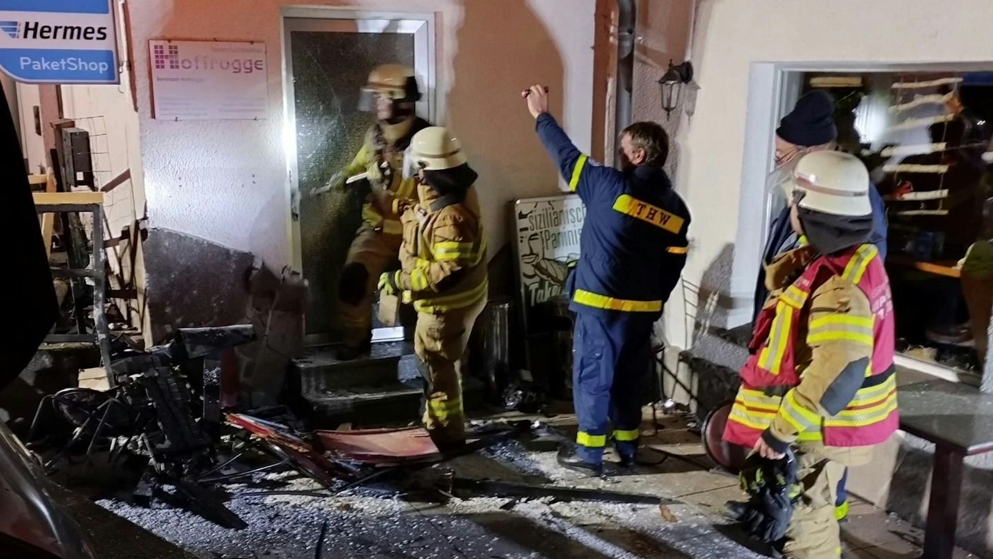 Feuerwehrleute und ein THW-Helfer stehen an einer schwer beschädigten Hauswand n Odenthal-Blecher.