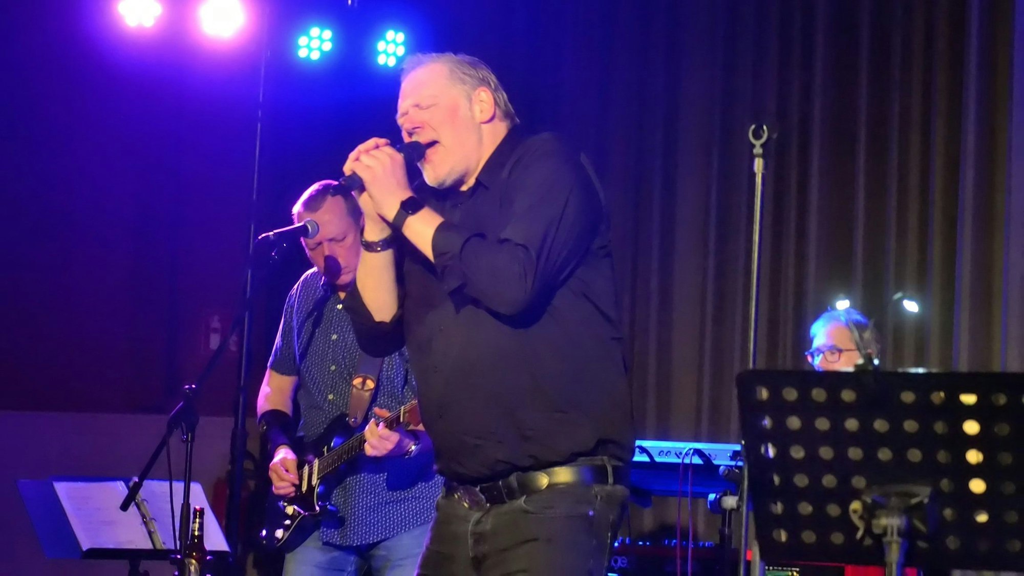 Ein Mann mit geschlossenen Augen sing in ein Mikrofon, das er mit beiden Händen nah vor seinen Mund hält.