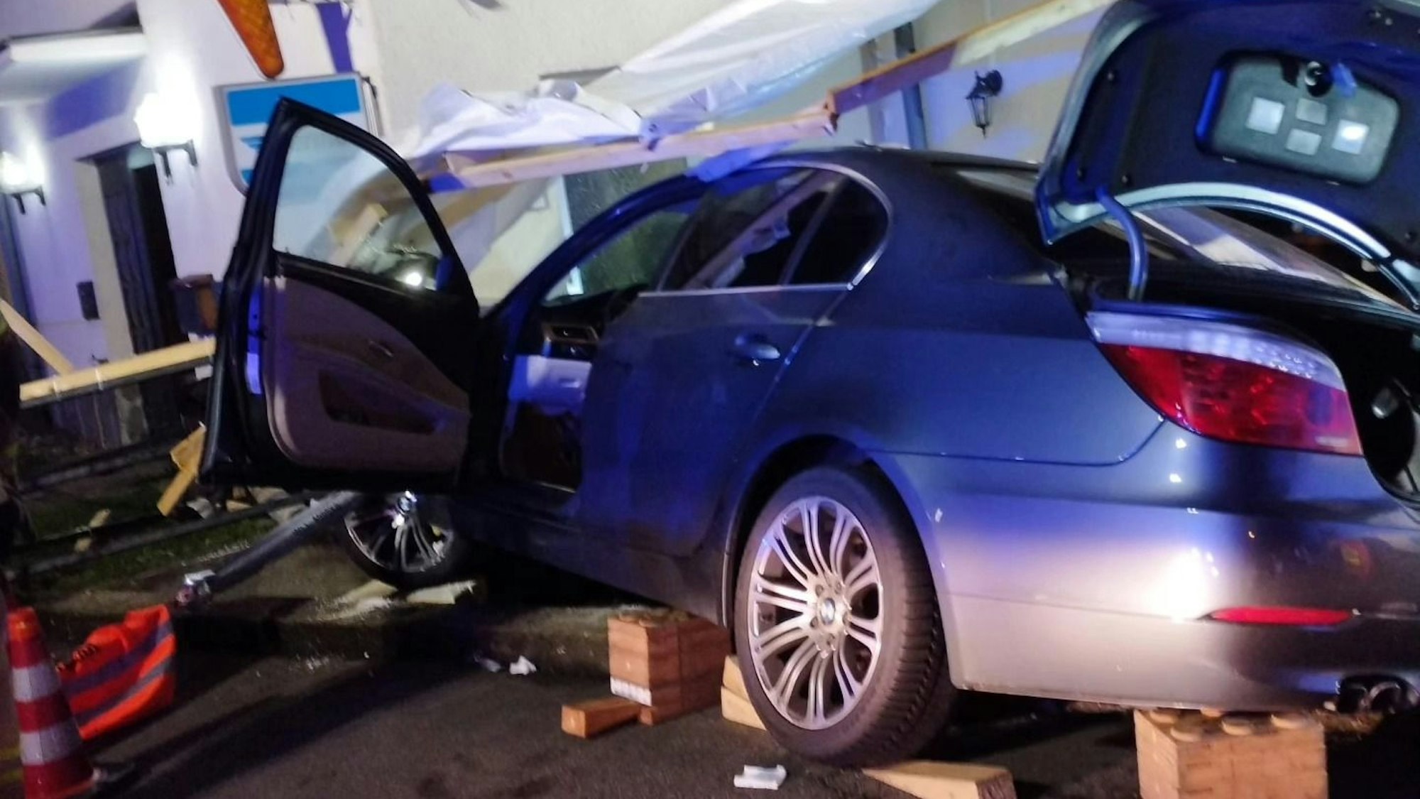 Ein schwer beschädigtes Unfallauto steht, von der Feuerwehr aufgebockt, vor einer Hauswand.