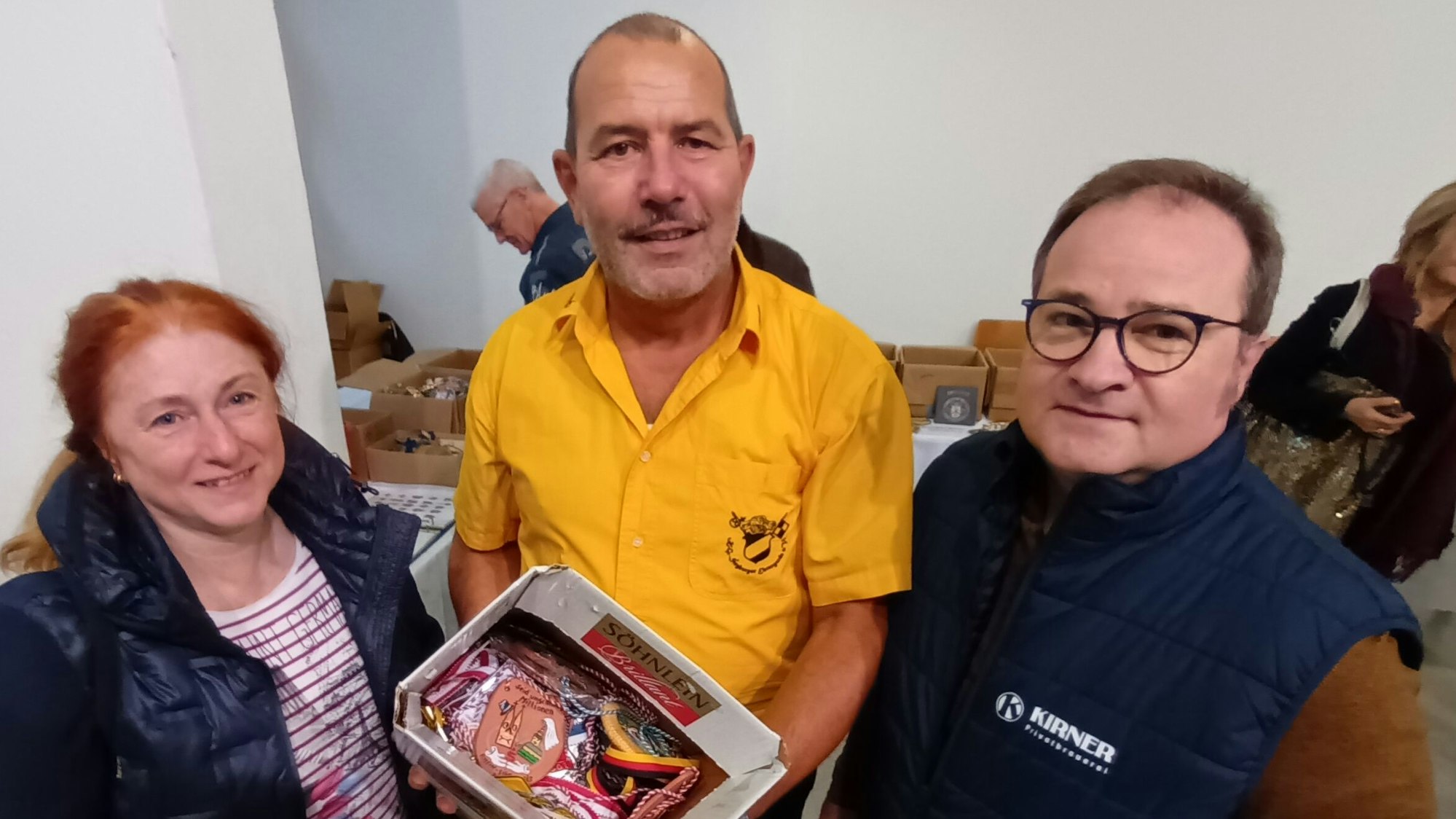 Zwei Männer und eine Frau mit einer Kiste voller Karnevalsorden