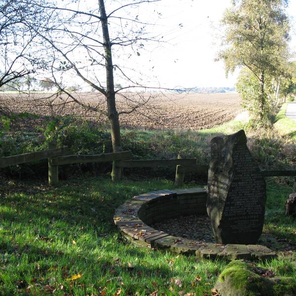 Blick auf einen frisch umgepflügten Acker mit dem Drei-Herren-Stein-Denkmal im Vordergrund.