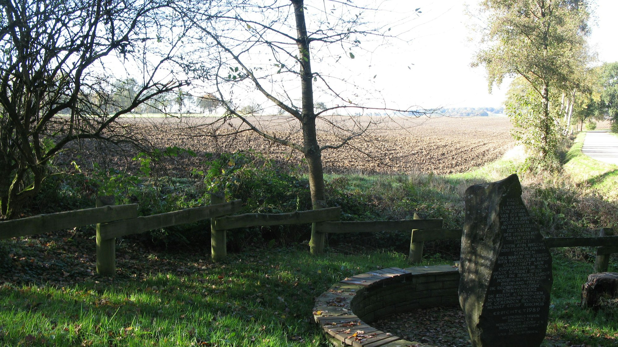 Blick auf einen frisch umgepflügten Acker mit dem Drei-Herren-Stein-Denkmal im Vordergrund.