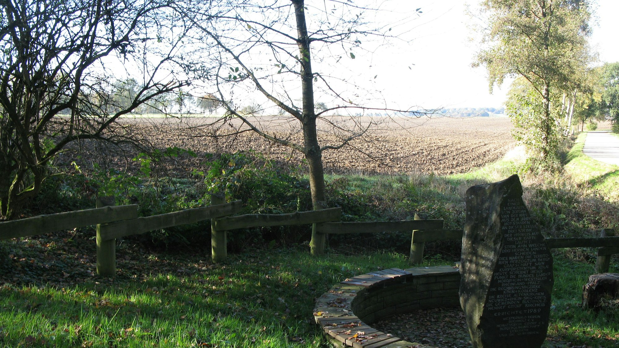 Blick auf einen frisch umgepflügten Acker mit dem Drei-Herren-Stein-Denkmal im Vordergrund.