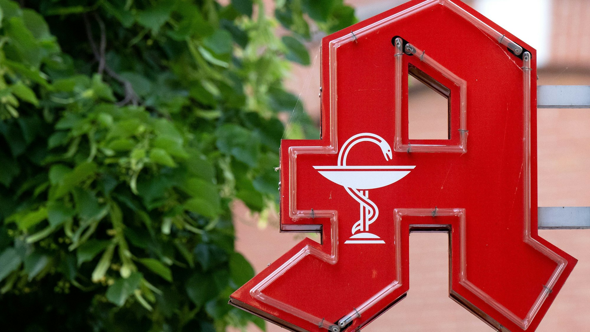 Das Logo einer Apotheke hängt an einem Gebäude.