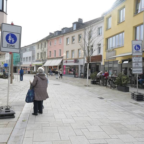 Rechts und links der Straße stehen die Verkehrsschilder Fußgängerzone. Eine Frau daneben.