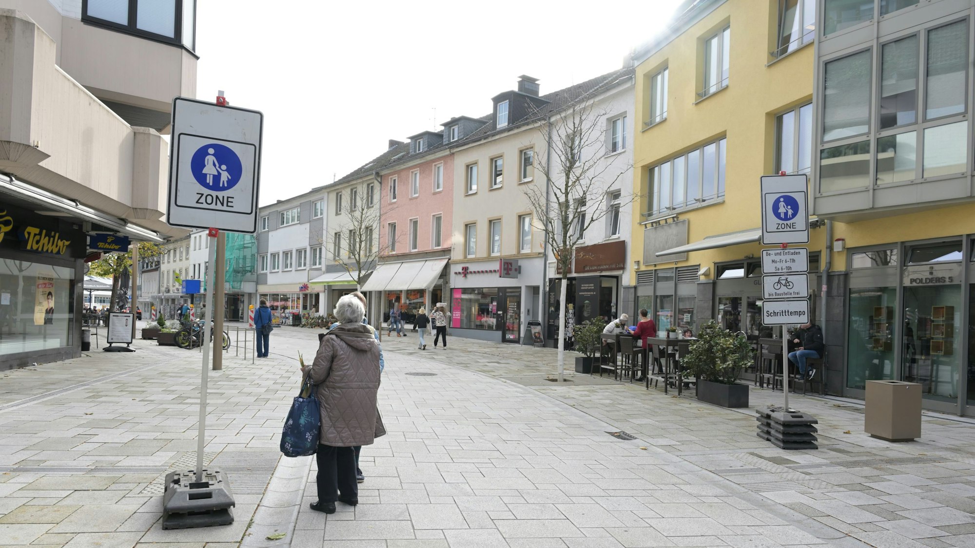 Rechts und links der Straße stehen die Verkehrsschilder Fußgängerzone. Eine Frau daneben.