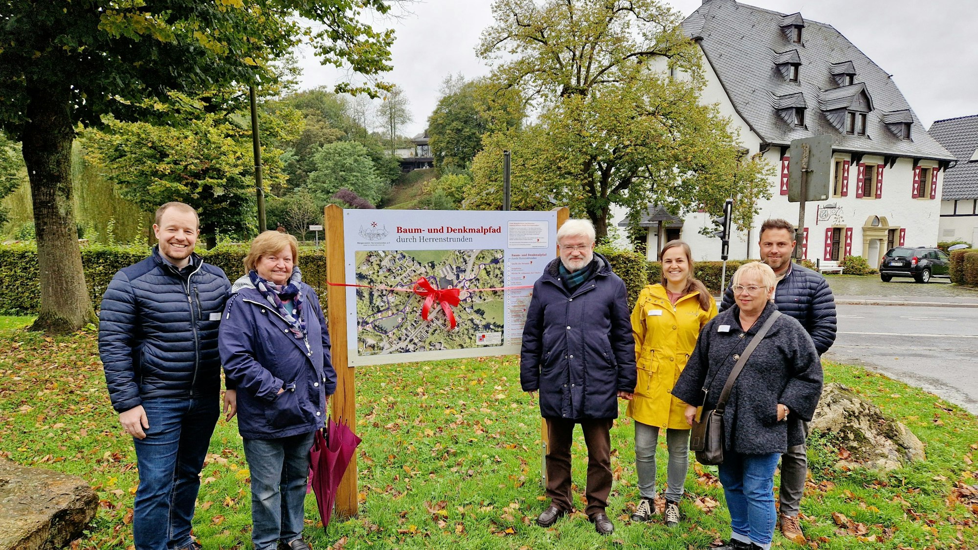 Sechs Menschen stehen an einer neuen Wandertafel vor der Malteser-Komturei in Herrenstrunden.