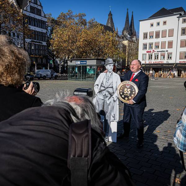 Personen mit Kameras in der Hand fotografieren Ralf Schlegelmilch der einen Pappaufsteller von Willi Ostermann im Arm hält.