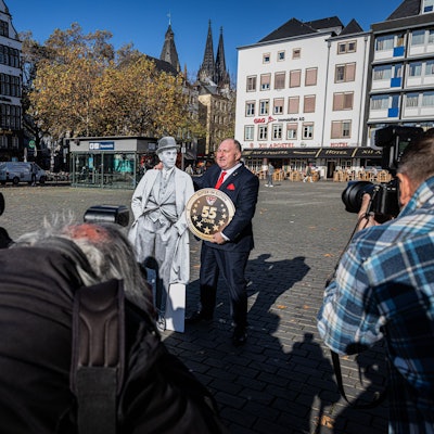 Personen mit Kameras in der Hand fotografieren Ralf Schlegelmilch der einen Pappaufsteller von Willi Ostermann im Arm hält.