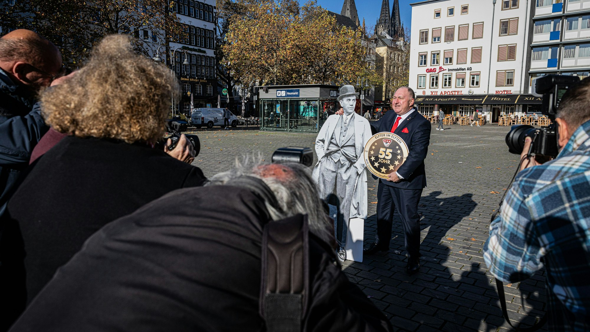 Personen mit Kameras in der Hand fotografieren Ralf Schlegelmilch der einen Pappaufsteller von Willi Ostermann im Arm hält.