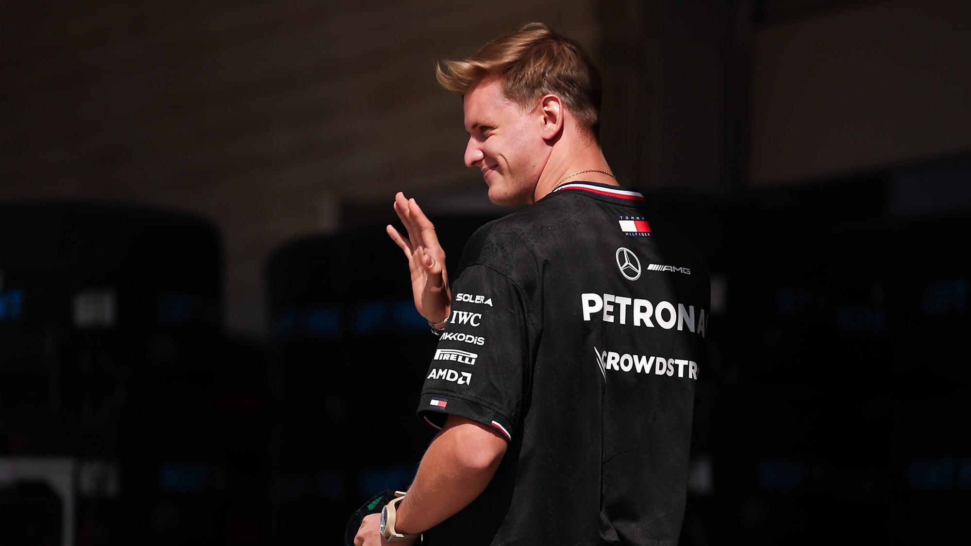 Mick Schumacher geht durch die Boxengasse und winkt.
