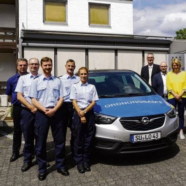 Elf Menschen gruppieren sich um ein Fahrzeug des Ordnungsamtes