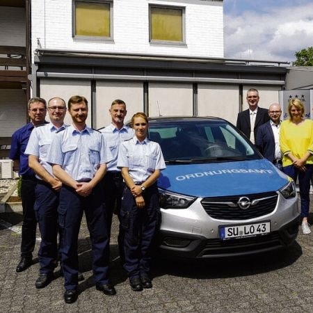 Elf Menschen gruppieren sich um ein Fahrzeug des Ordnungsamtes