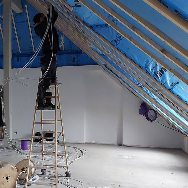 Zwei Handwerker arbeiten im Dachgeschoss eines Hauses. Einer der Männer steht auf einer Leiter.